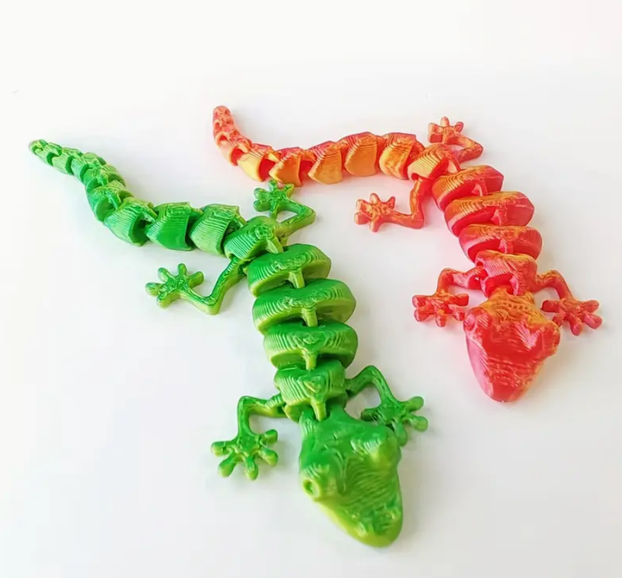 Two plastic gecko toys, one green and one red, on a white background