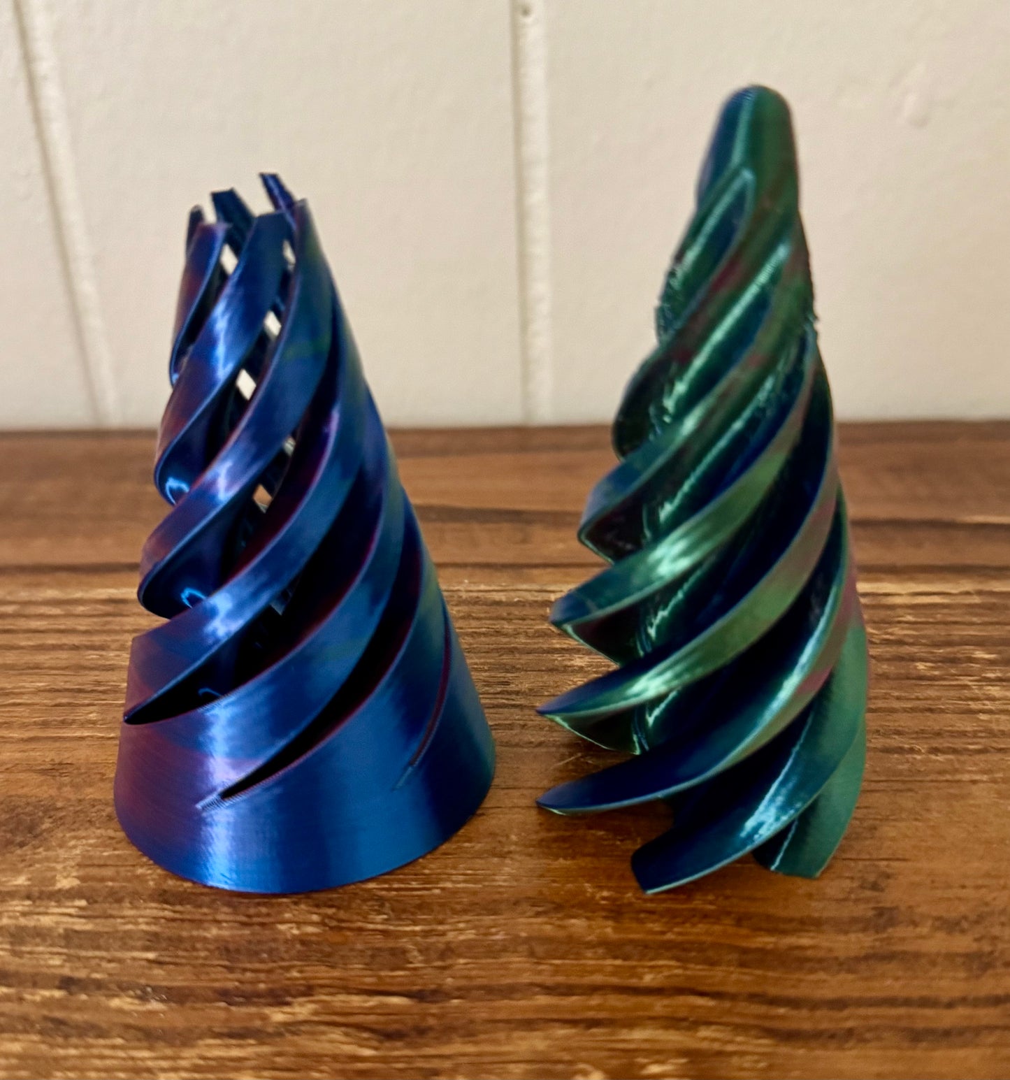 Two metallic spiral-shaped objects on a wooden surface with a white paneled wall background.