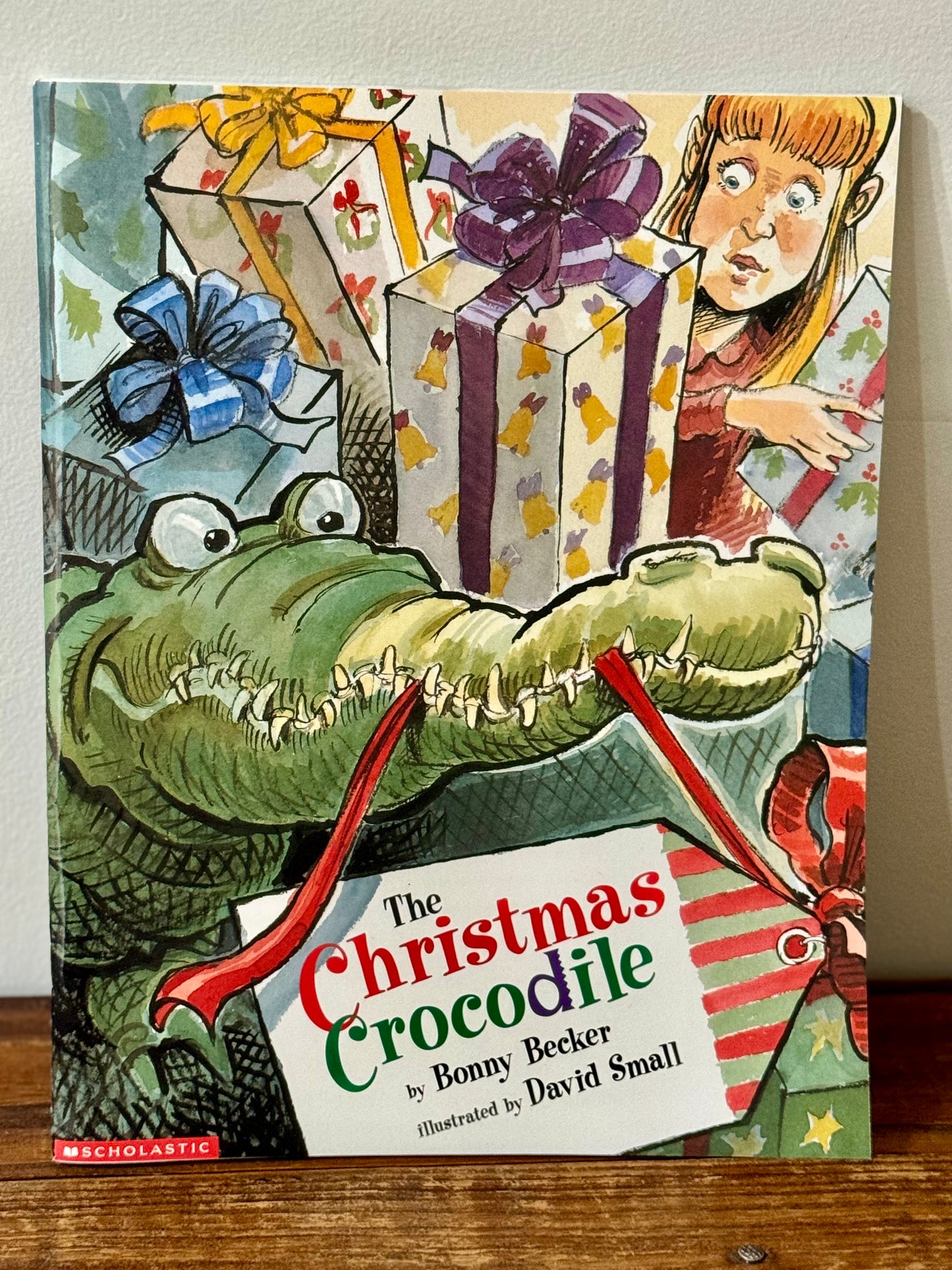 Cover of The Christmas Crocodile by Bonny Becker, featuring a mischievous crocodile adorned with a red bow under a Christmas tree.