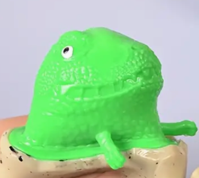 Green dinosaur-shaped object on a cork surface with a light purple background
