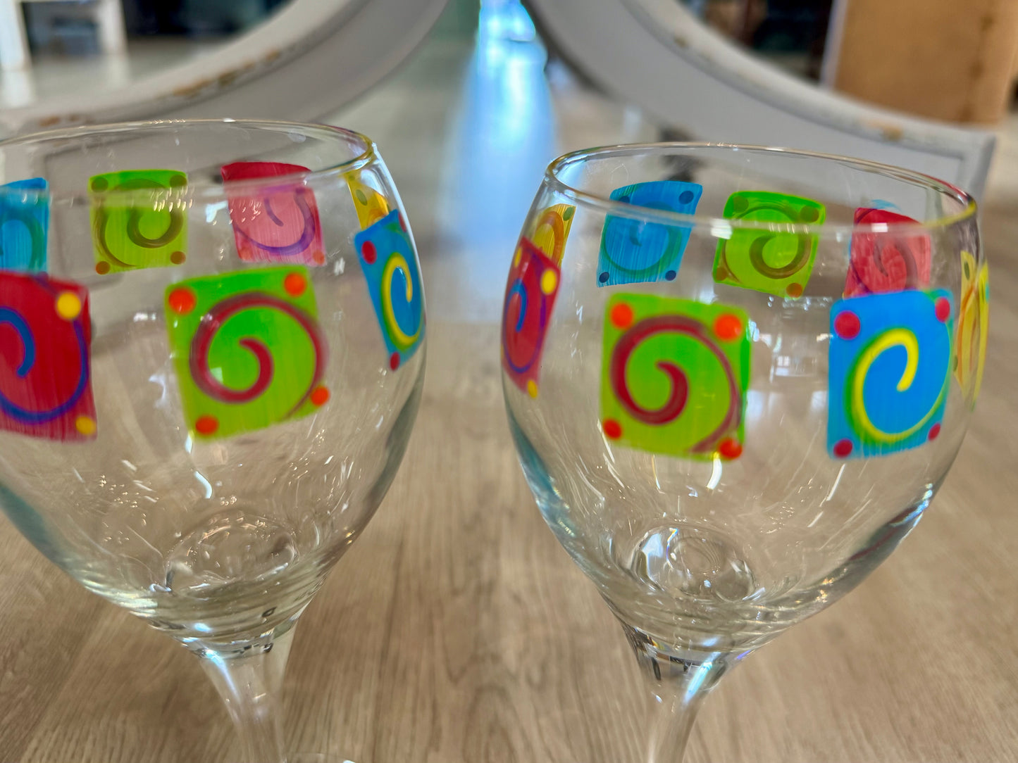 Pair of hand-painted wine glasses featuring colorful swirl square designs and signed glass bases