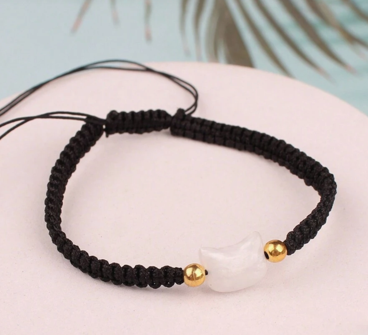 Black braided bracelet with gold beads on a light pink surface