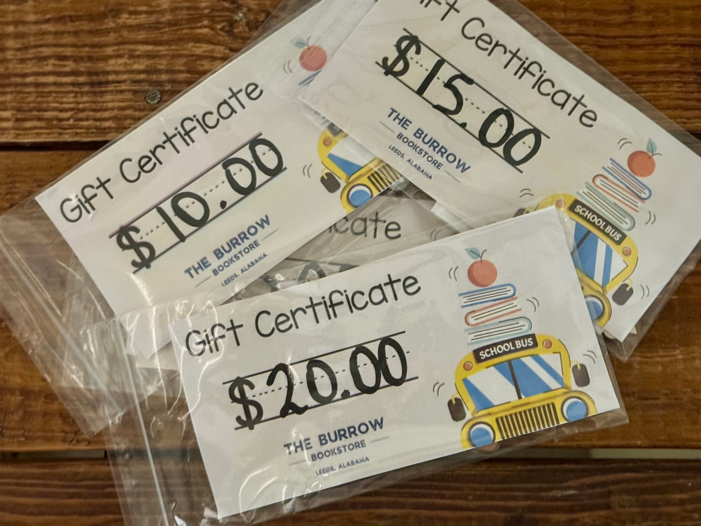 Three gift certificates for 'The Burrow Bookstore' on a wooden surface.