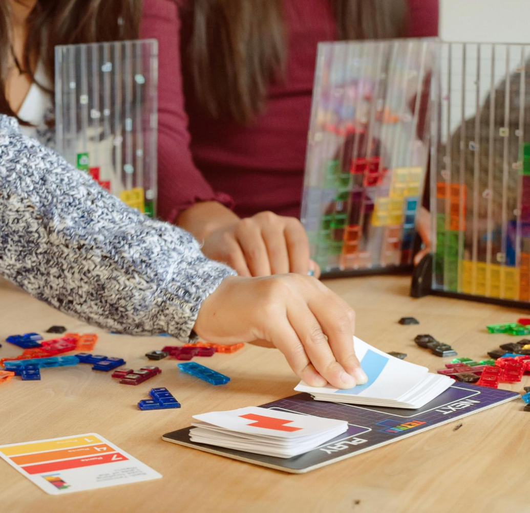 Two people playing a board game with colorful pieces on a wooden table.