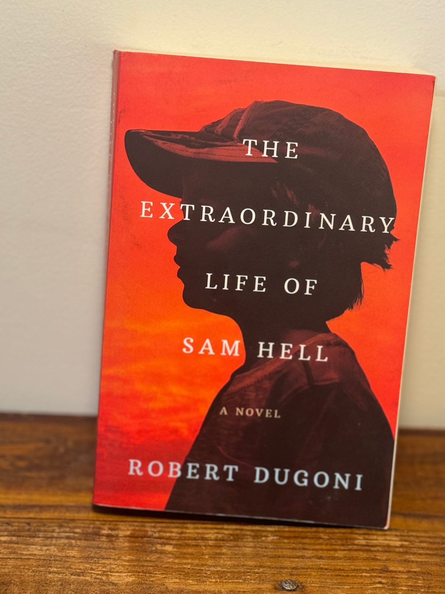 Cover of The Extraordinary Life of Sam Hell by Robert Dugoni, depicting a young boy with striking red eyes against a backdrop of a school setting.