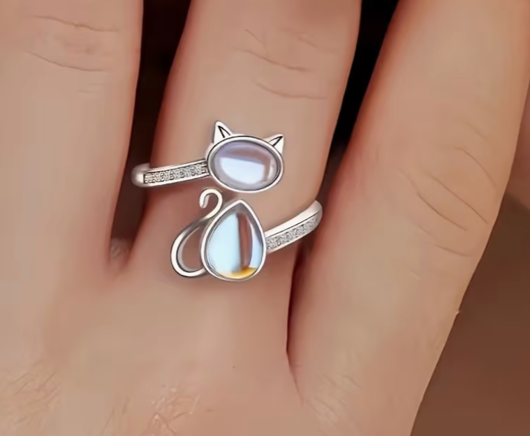 Adjustable silver tone cat ring with opal glass stones shown worn on finger, featuring an open wrap design and minimalist cat silhouette