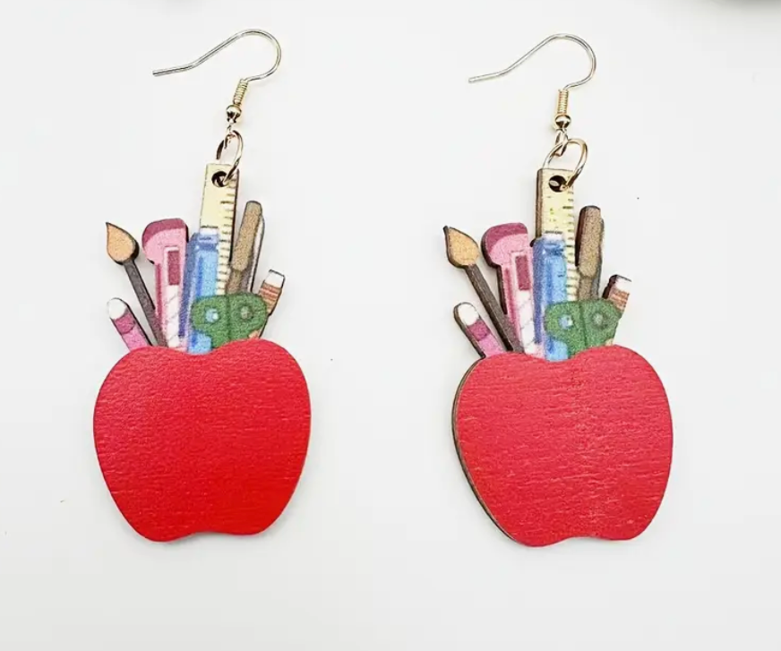 Pair of wooden earrings shaped like apples filled with tiny school supplies including rulers, scissors, and paint brushes—perfect for teachers and educators.
