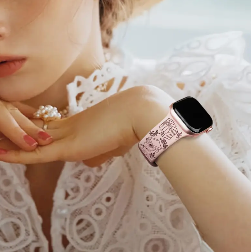 Close-up of a person's wrist wearing a smartwatch with a decorative band, holding a pearl ring.