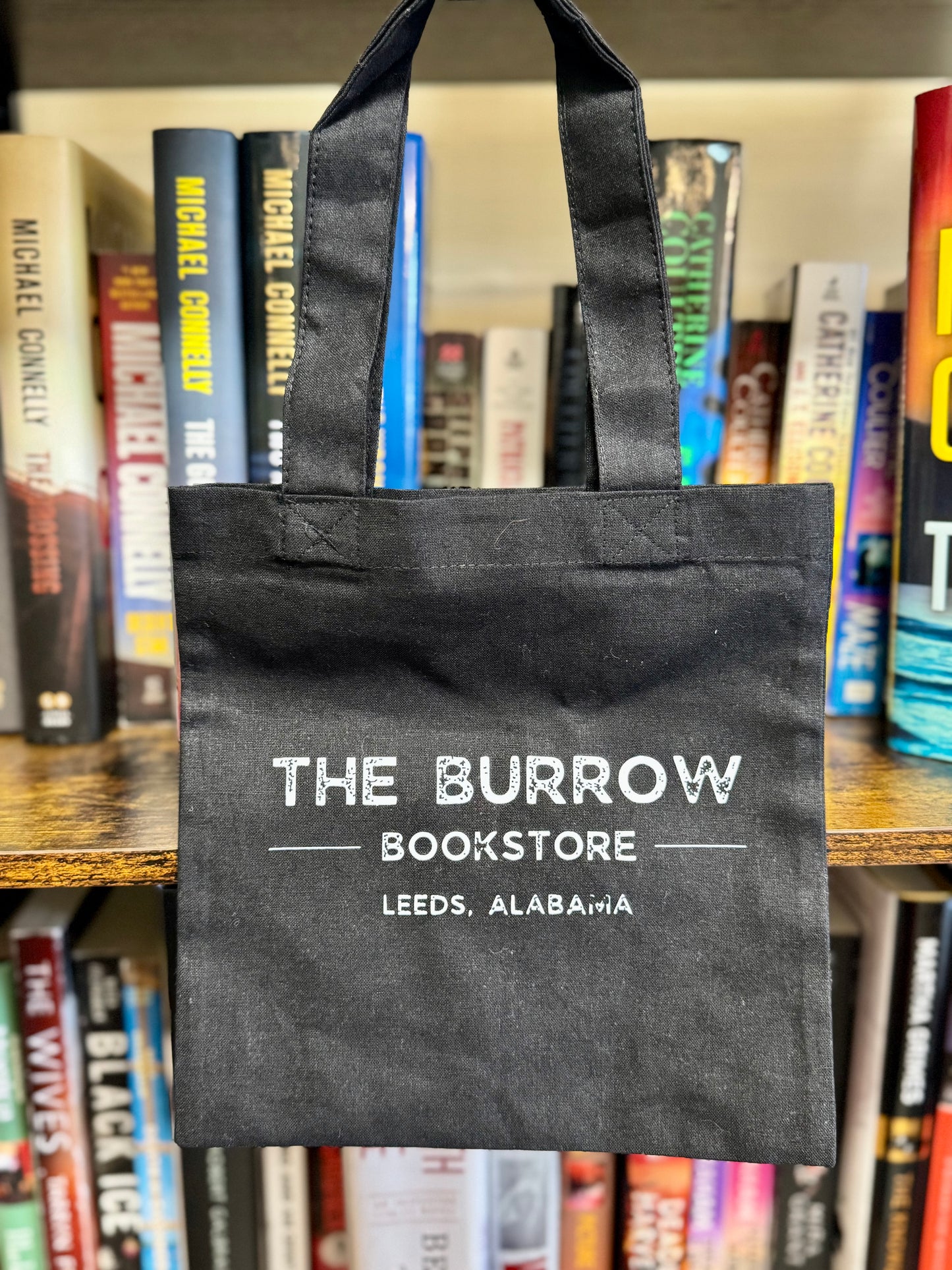 Small natural canvas tote bag with Be Happy It Drives People Crazy and a dandelion being blown to make a wish on one side, and The Burrow Bookstore on the other side.