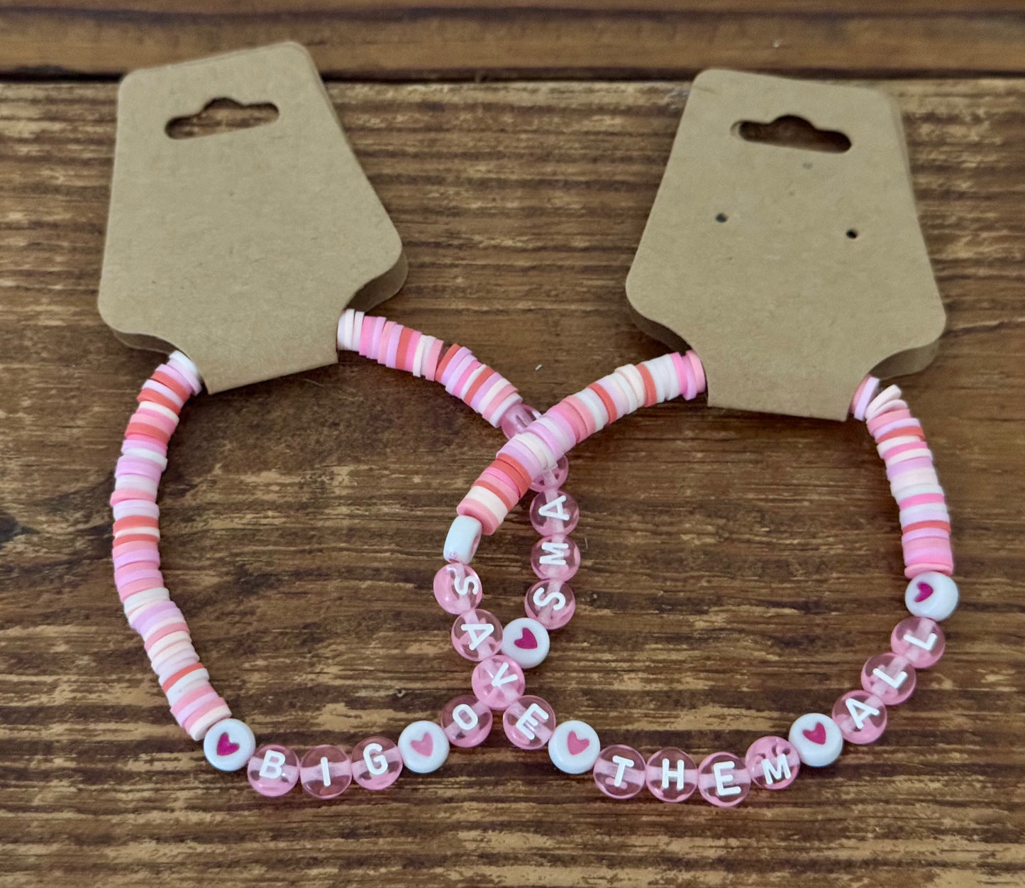Two pink beaded bracelets on a wooden surface with cardboard holders.