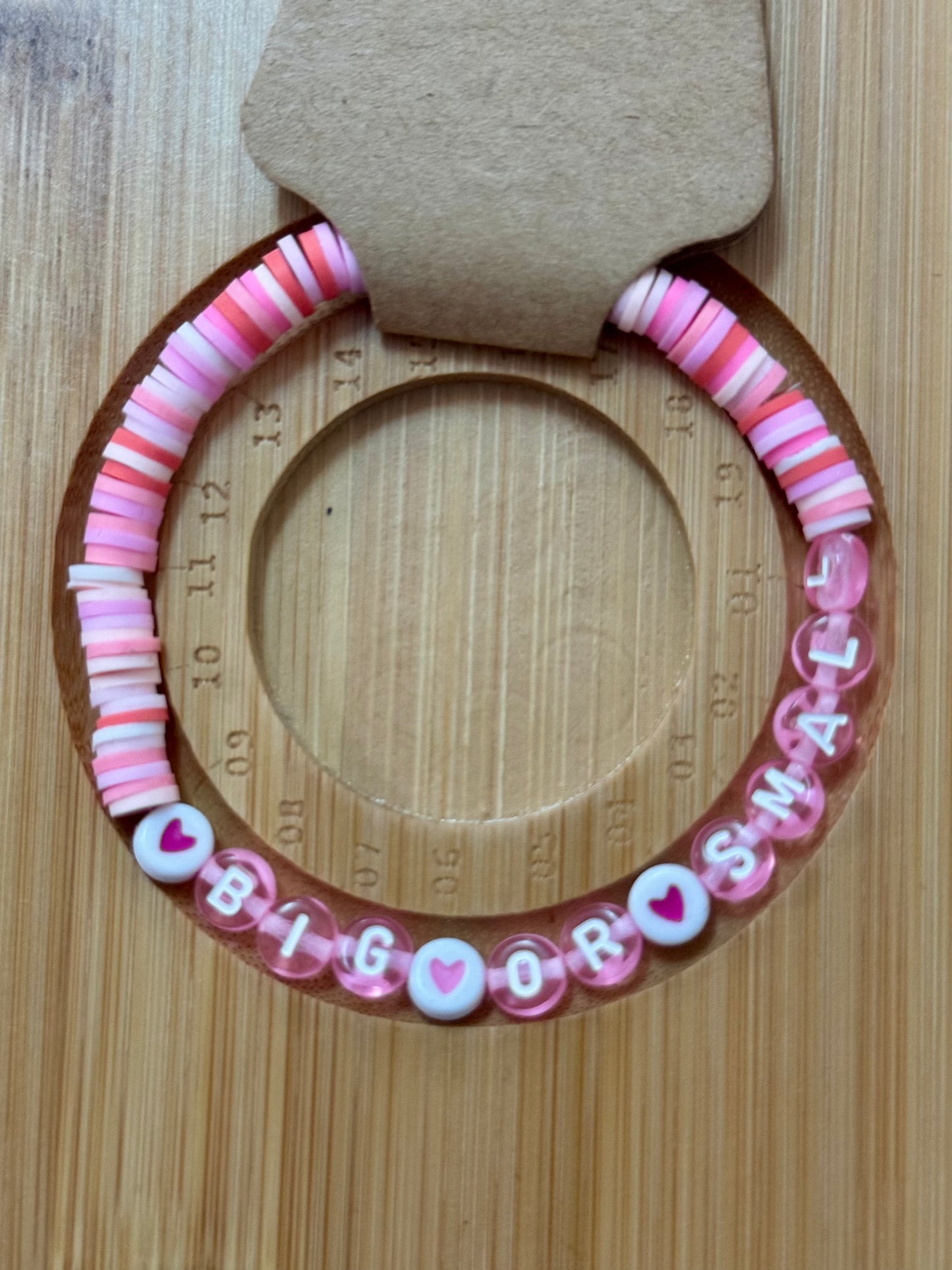 Pink and white beaded bracelet with 'BIG BROTHER' text on a wooden surface