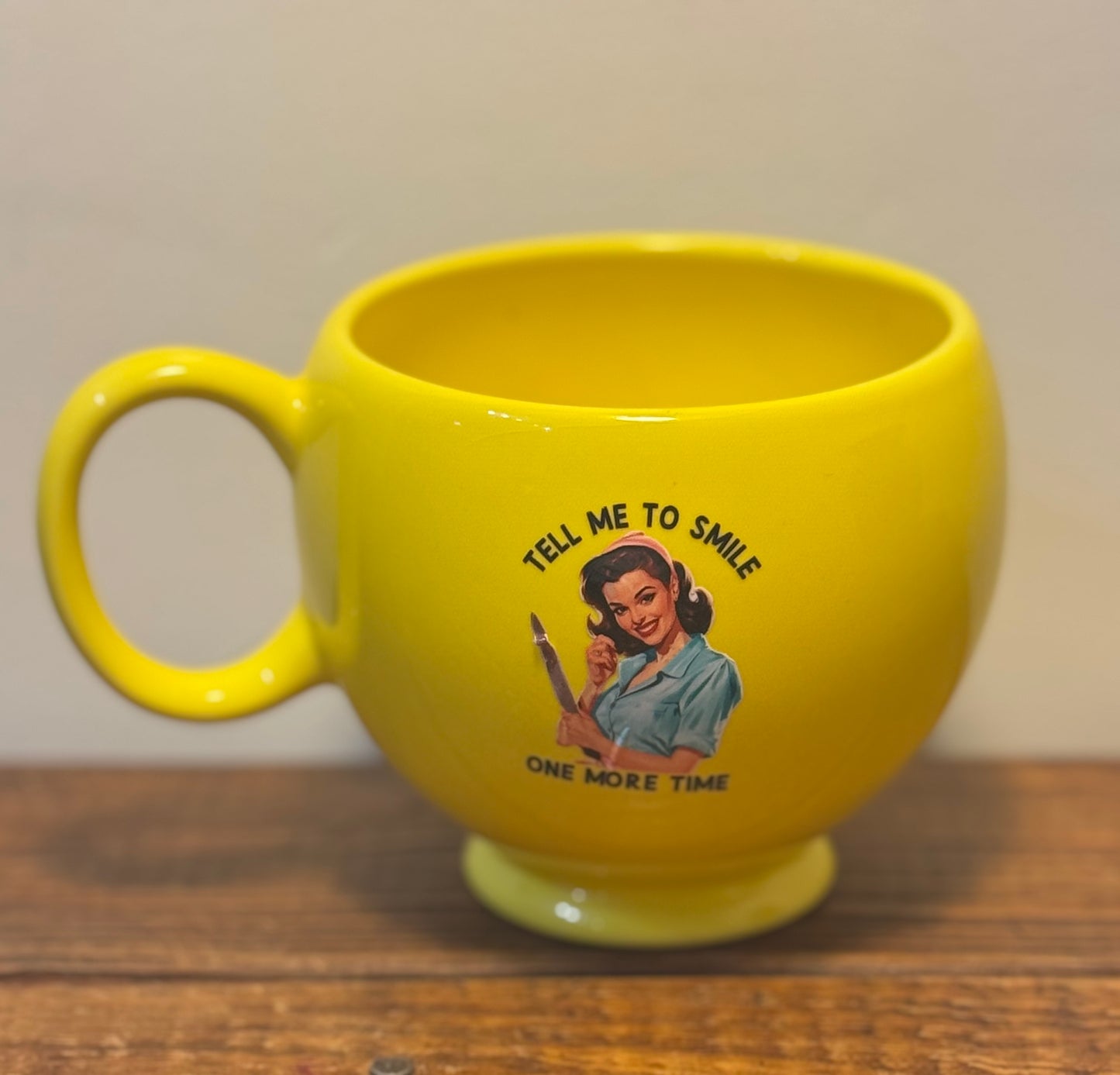 Large yellow mug with a smiley face on the front and a retro 1950s housewife on the back, saying Tell me to smile one more time.