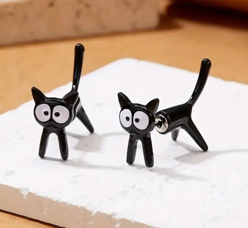 Black cat-shaped earrings on a white surface with a wooden background