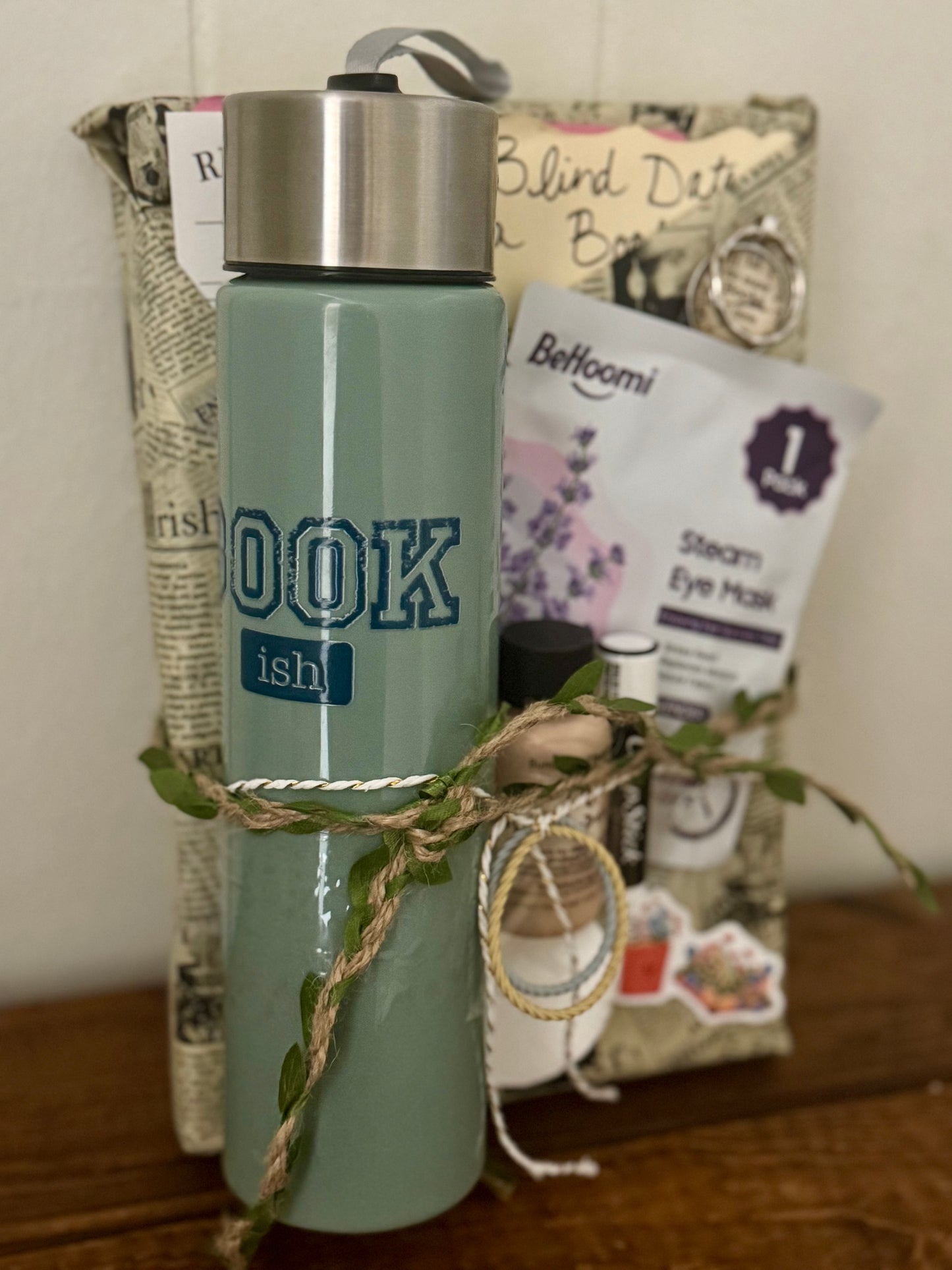 Green water bottle with 'BOOK ish' text, surrounded by small items on a wooden surface.