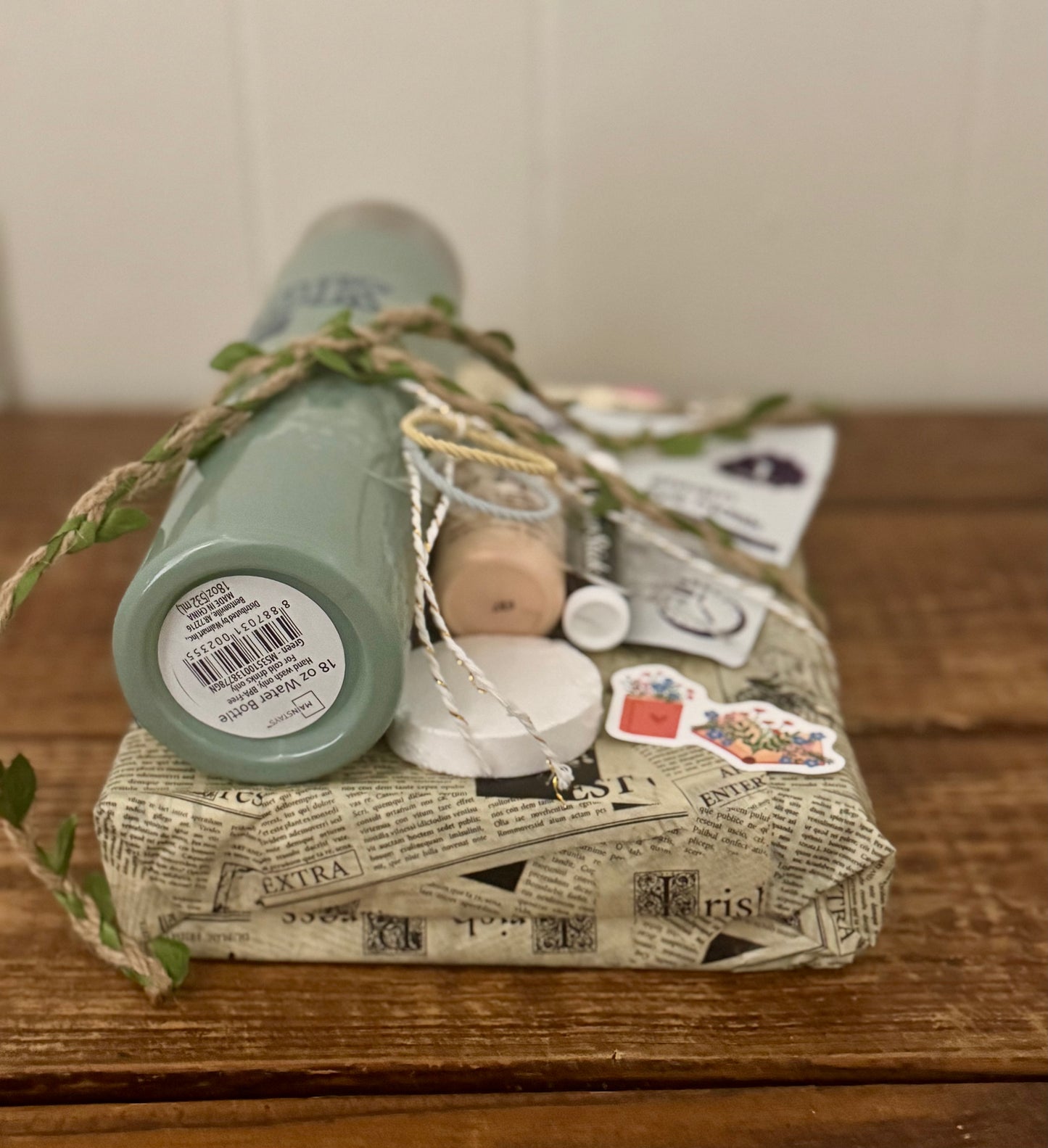 Green bottle wrapped in newspaper with decorative elements on a wooden surface