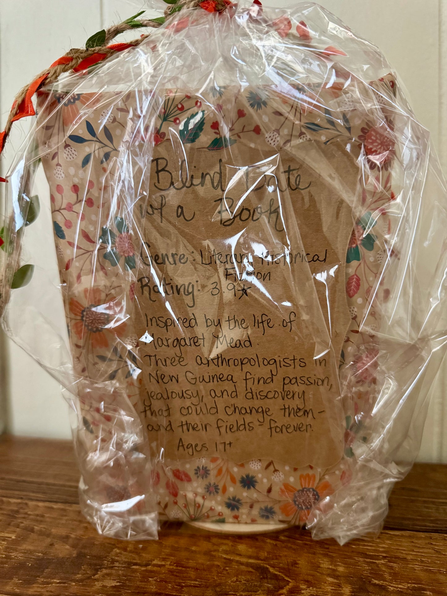 Decorative item wrapped in clear plastic with a brown paper label on a wooden surface.