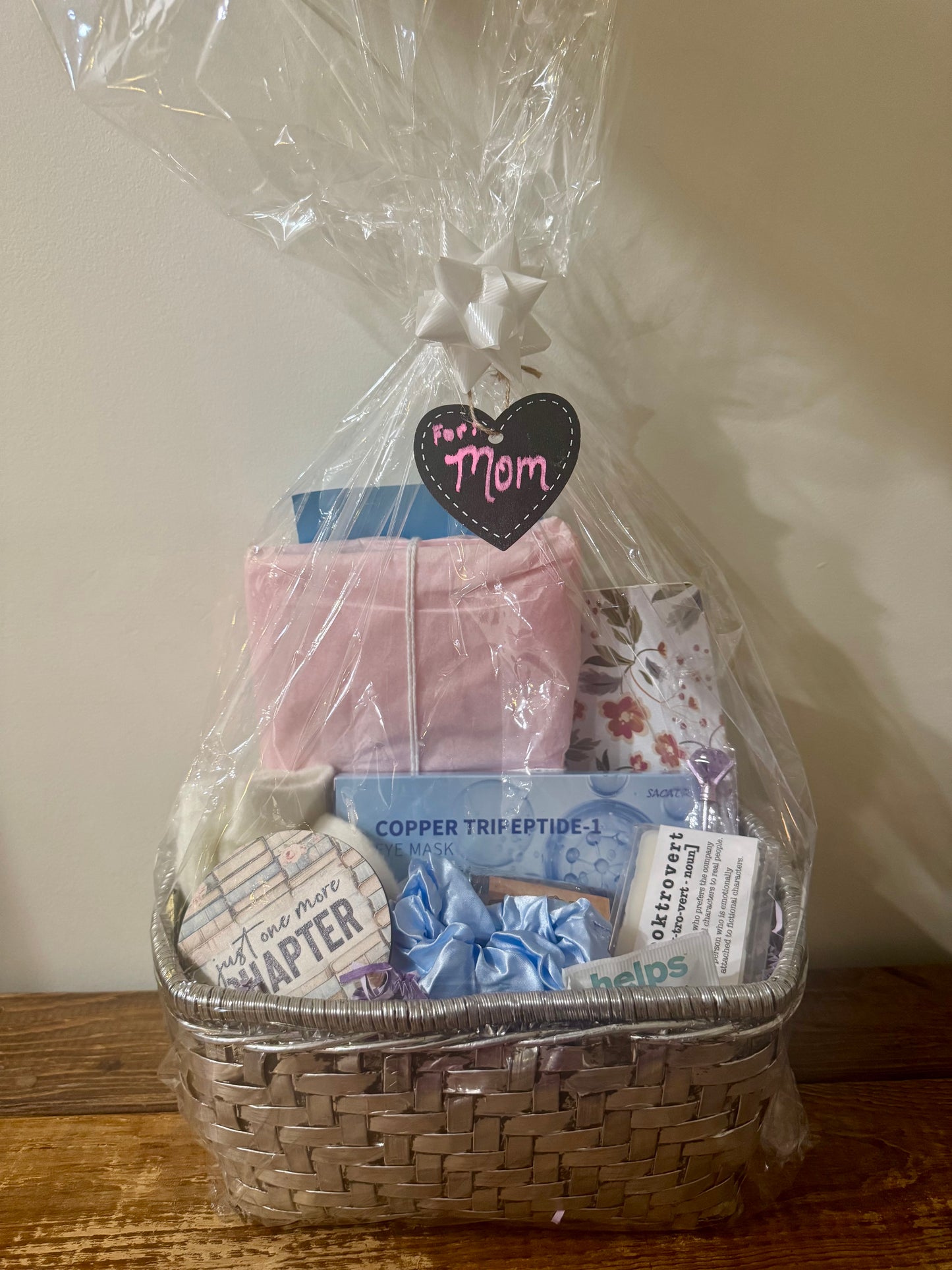 Gift basket for mom featuring a blind date with a book (romantic mystery), journal, pen, eye mask, fuzzy socks, tea, wax melts, scrunchie, hand sanitizer, and a coaster.