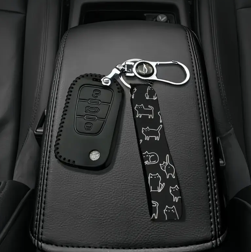 Car key fob cover and keychain with cat pattern on a car seat.