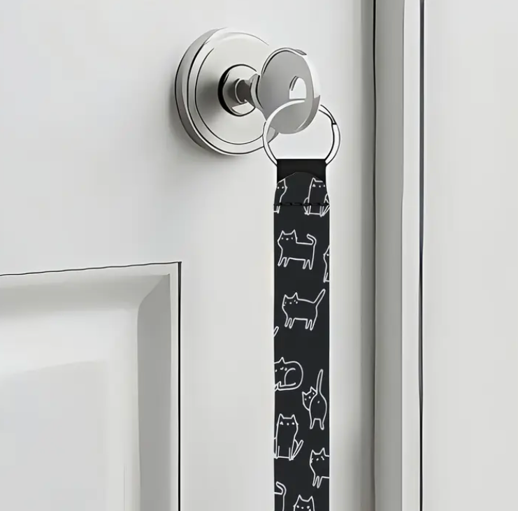 Key with a black keychain featuring white cat illustrations attached to a silver doorknob on a white door.