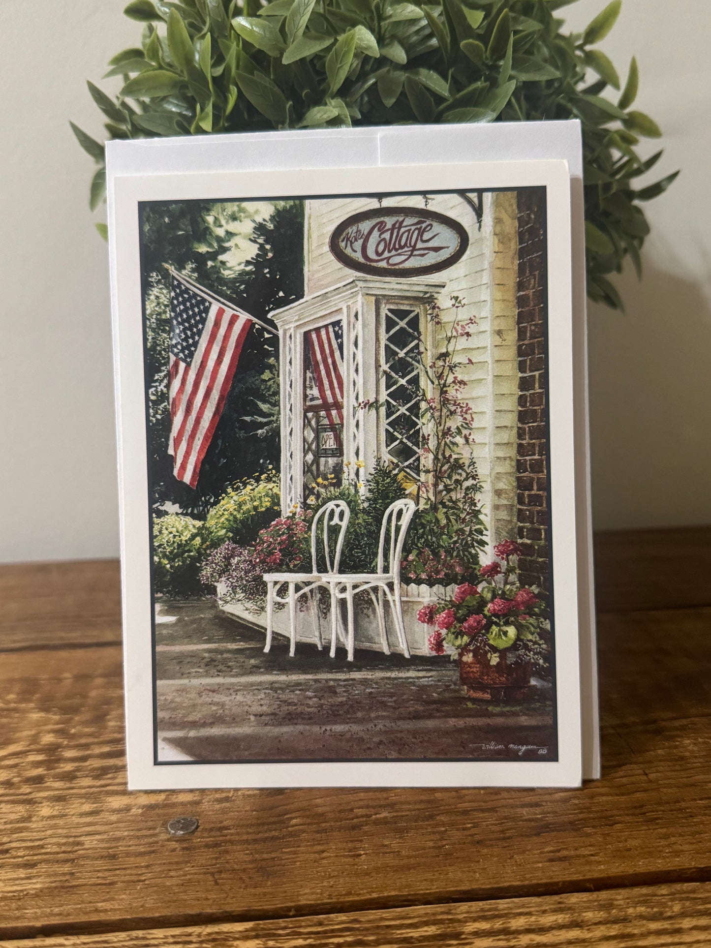 A charming notecard featuring a Southern country-style cottage in a summer setting, with an American flag in the background.
