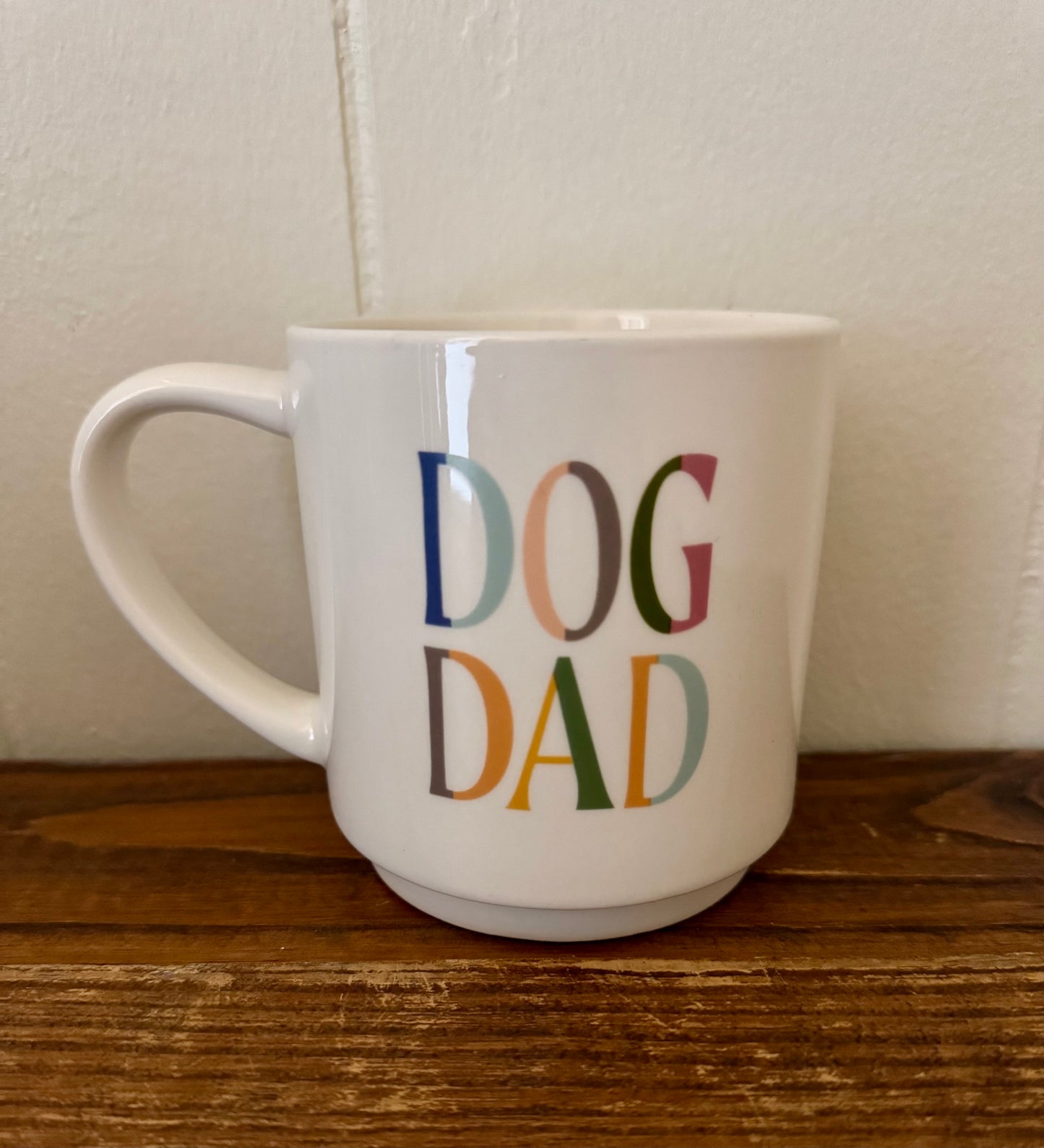 White mug with 'DOG DAD' in colorful letters on a wooden surface.