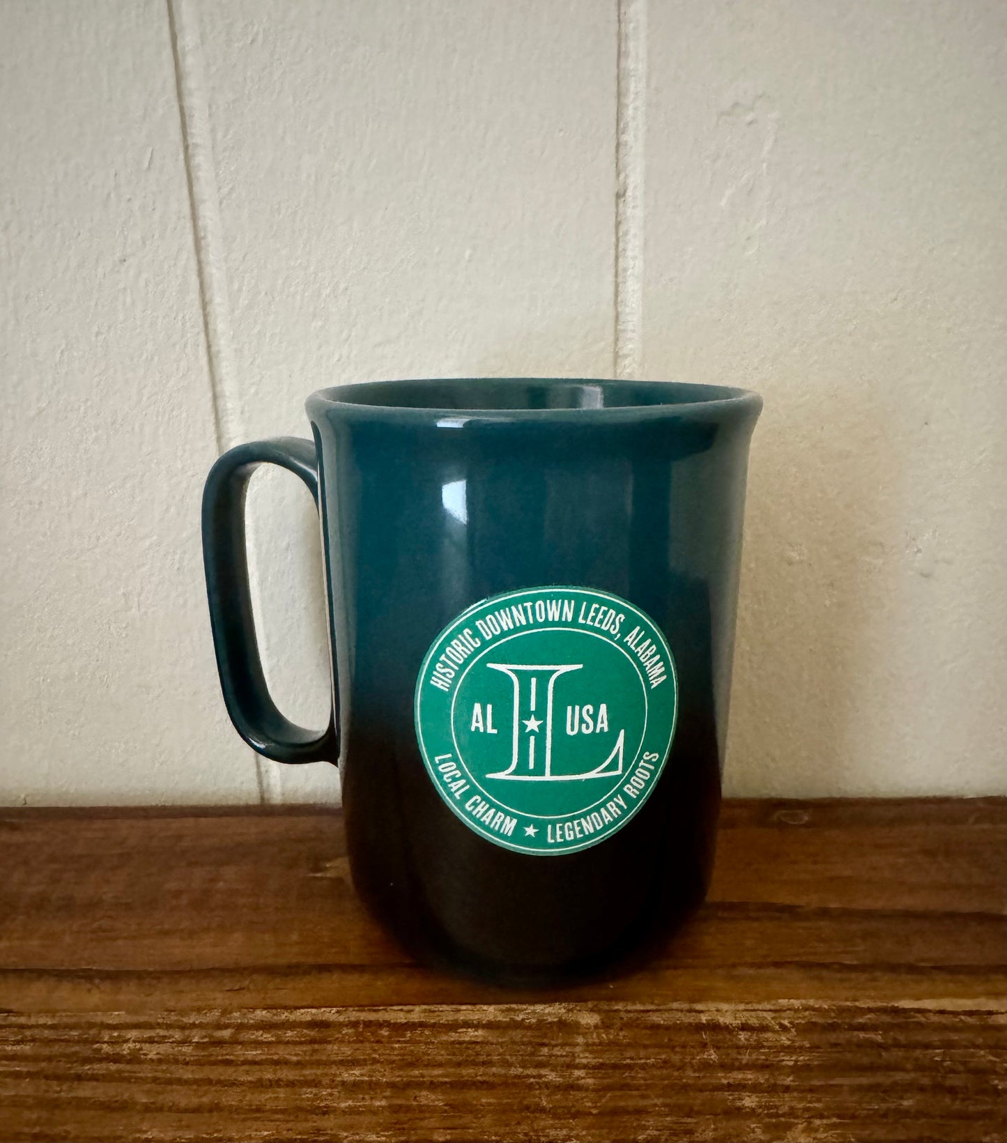 Green mug with a logo on a wooden surface and light-colored wall background