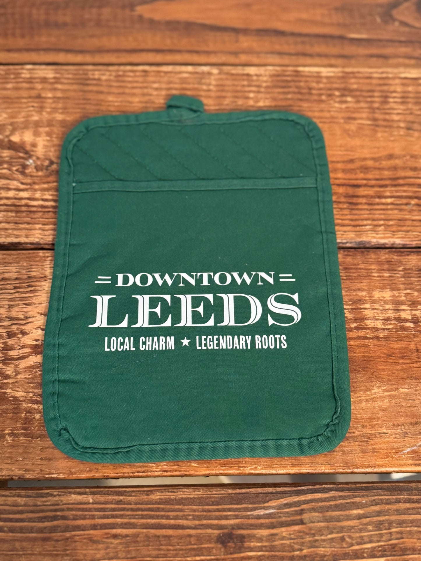 Green pot holder with 'Downtown Leeds' text on a wooden surface