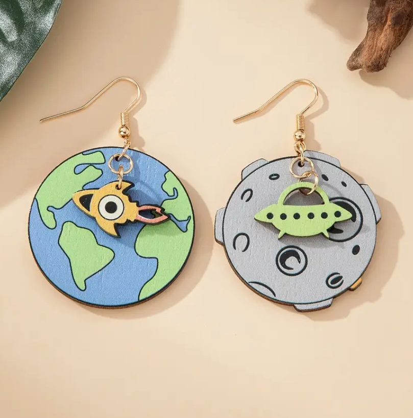 Pair of mismatched wooden earrings—one shaped like planet Earth with a dangling UFO, the other shaped like the moon with a dangling alien, perfect for space and sci-fi lovers.
