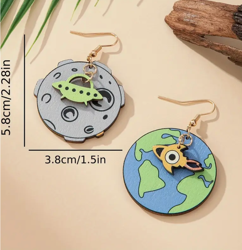 Pair of mismatched wooden earrings—one shaped like planet Earth with a dangling UFO, the other shaped like the moon with a dangling alien, perfect for space and sci-fi lovers.