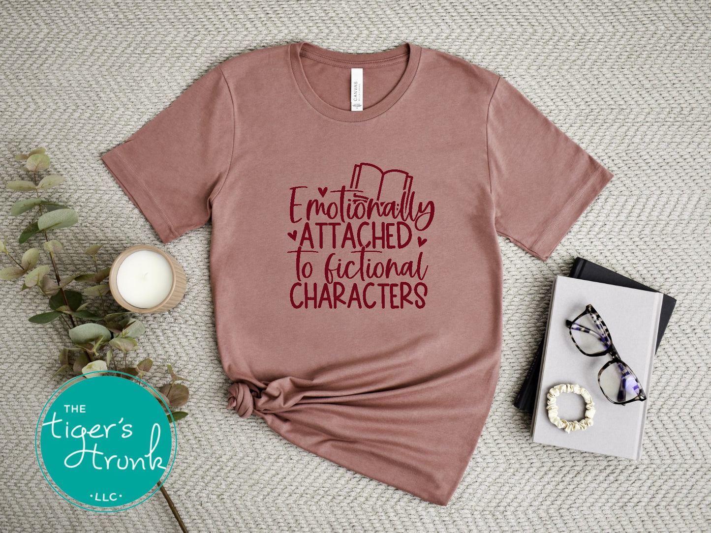 Mauve t-shirt with red text 'Emotionally Attached to Fictional Characters' on a textured surface with decor items.