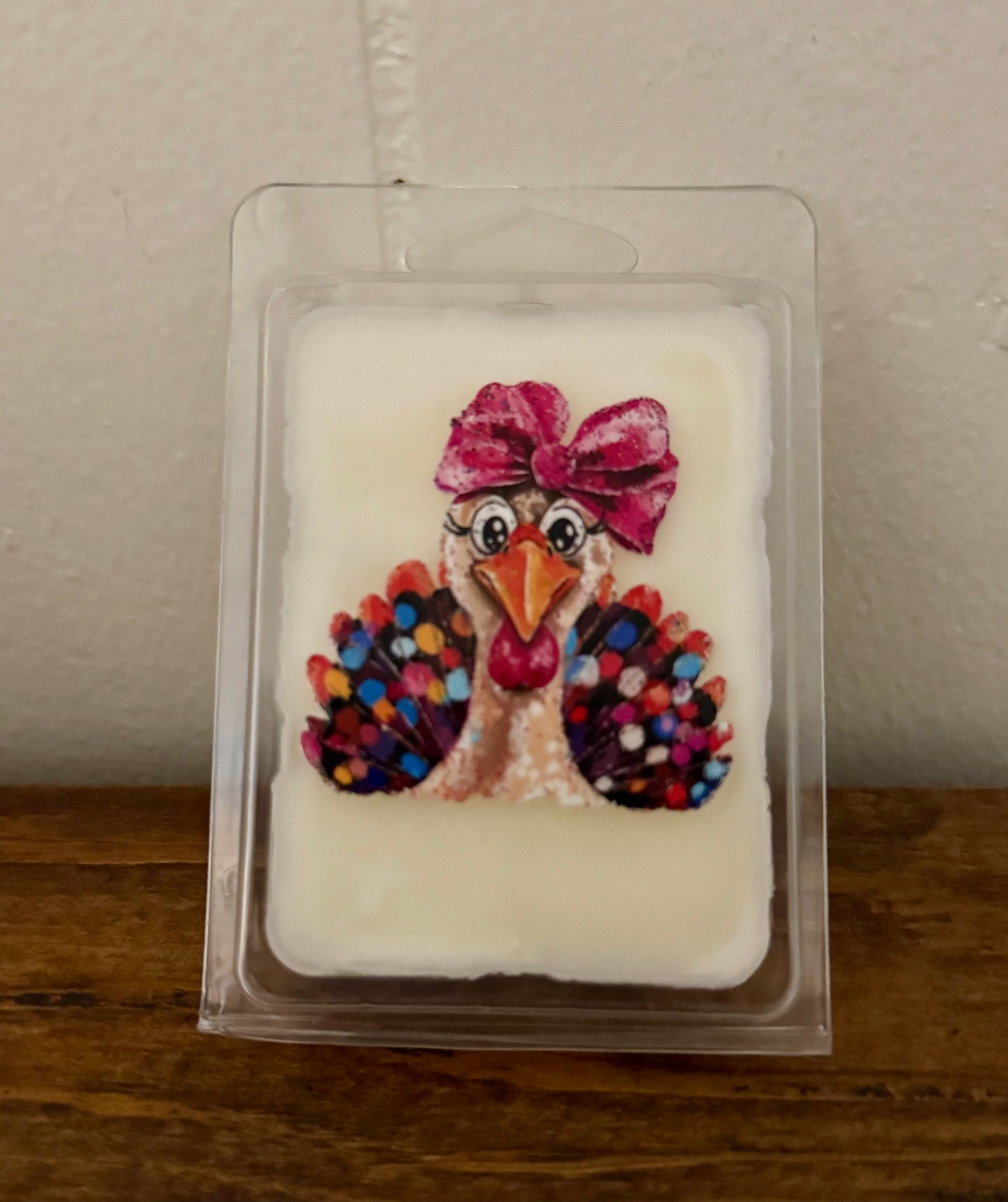 Candle melt block with a turkey design and colorful eggs on a clear plastic packaging against a beige background.