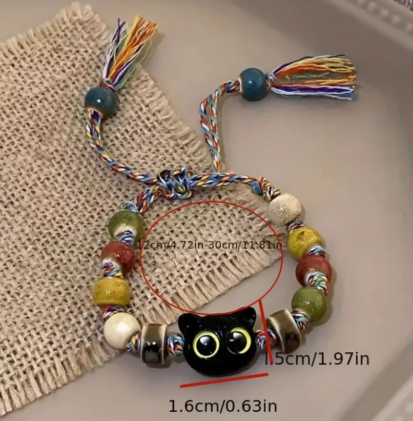 Colorful beaded bracelet with a black cat charm on a textured surface
