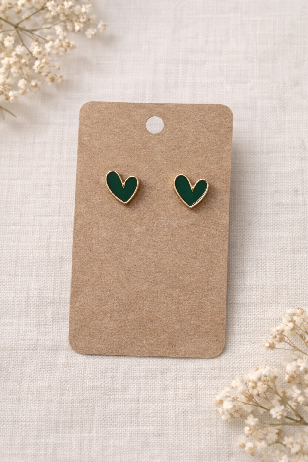 Green heart stud earrings with gold tone outline displayed on a neutral card with a soft background