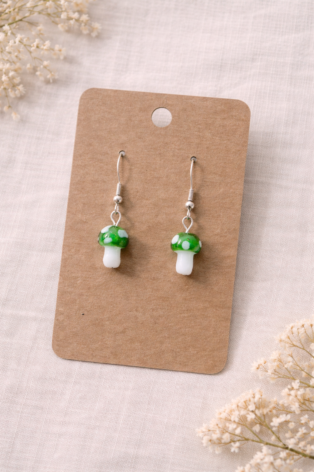 Green mushroom drop earrings with silver tone hooks displayed on a neutral jewelry card