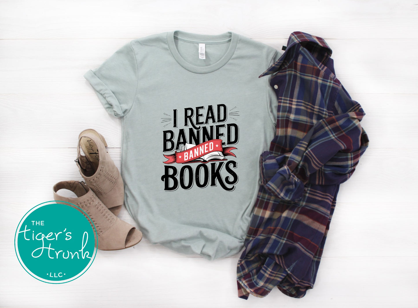 Light blue t-shirt with 'I Read Banned Books' text, plaid jacket, and shoes on a white background with 'The Tiger's Trunk' logo.