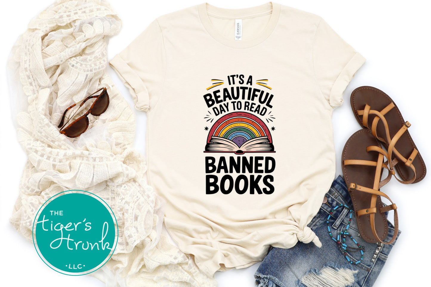 Beige t-shirt with 'It's a Beautiful Day to Read Banned Books' design, sunglasses, scarf, and sandals on a white background.