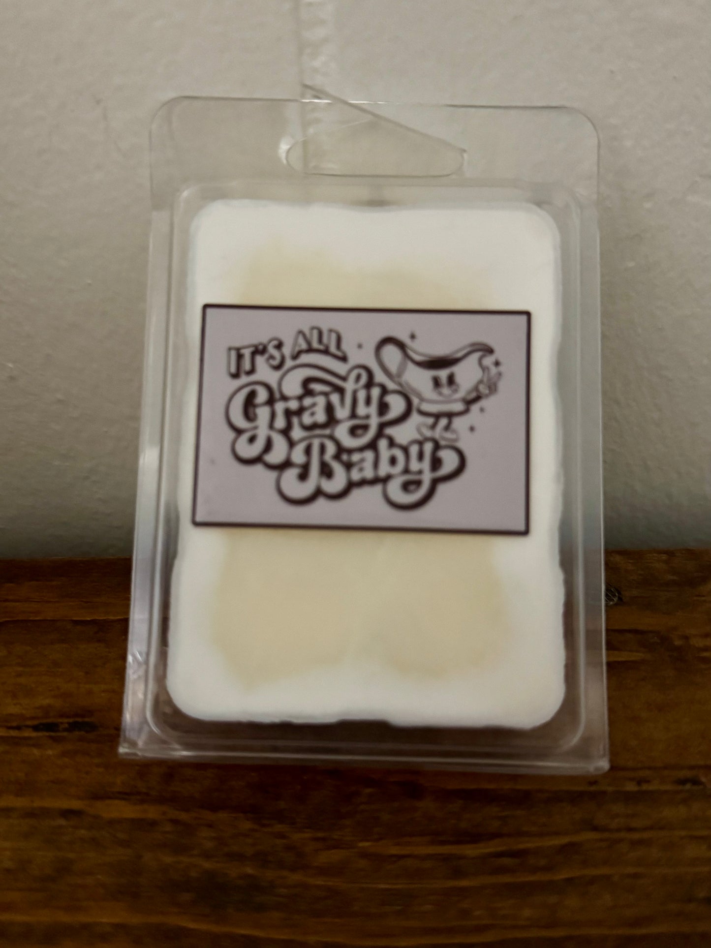 White block of soap in clear packaging with 'It's All Gravy Baby' label on a wooden surface.