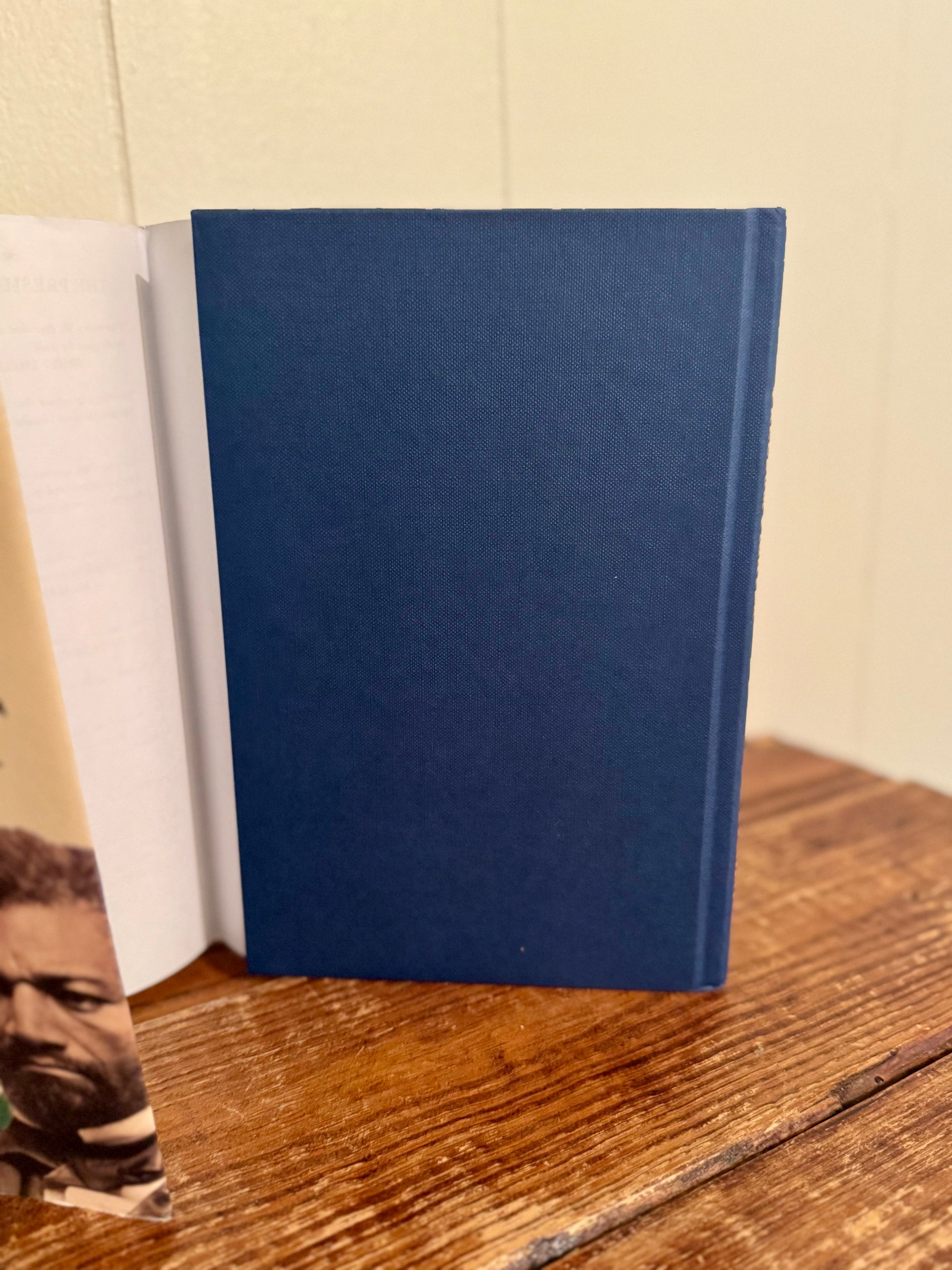 Blue notebook on a wooden surface with a white book and photo in the background