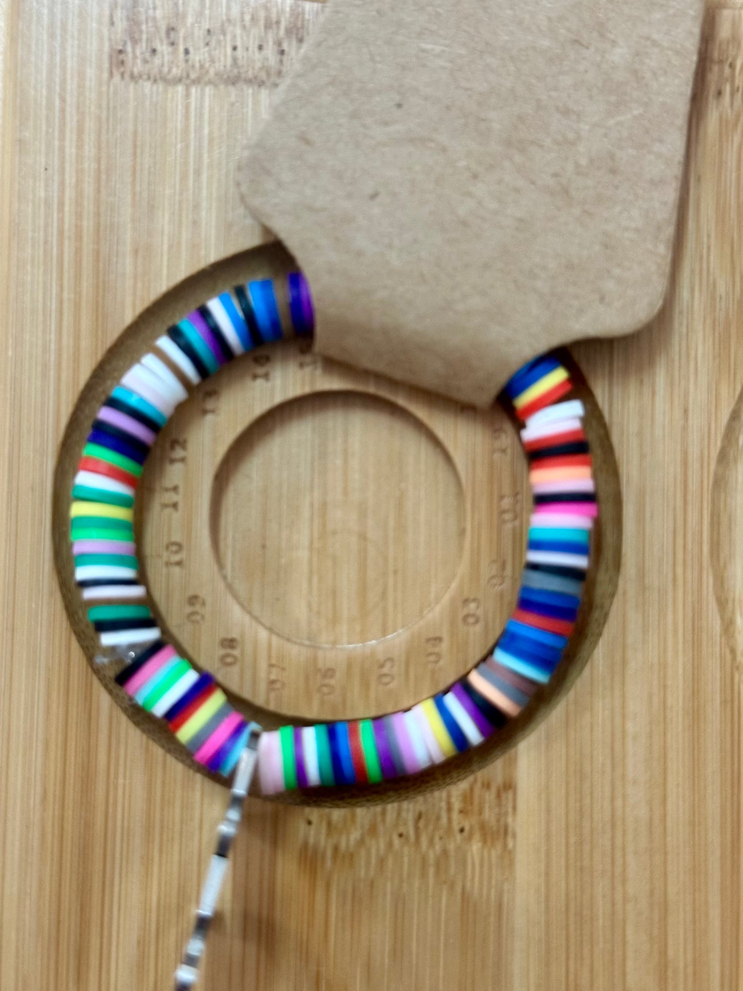 Colorful striped earrings on a wooden surface with a cardboard backing.