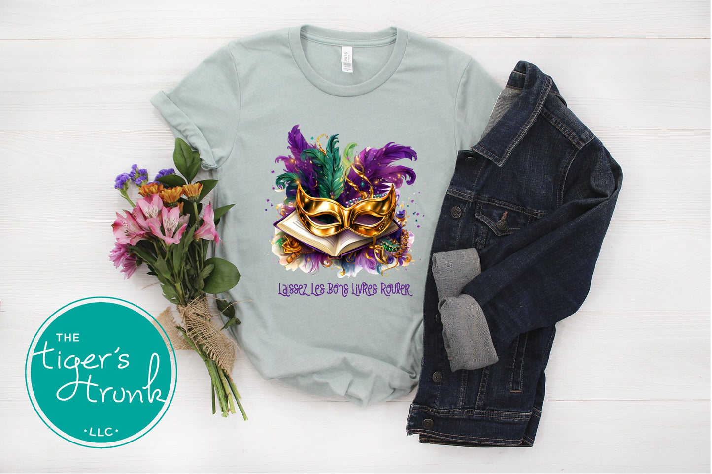 Light blue t-shirt with Mardi Gras mask design, flowers, and denim jacket on a white background.