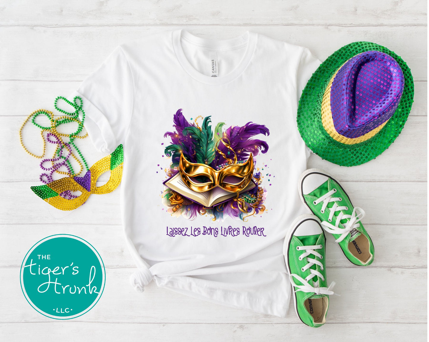 Mardi Gras-themed sweatshirt with mask design, green shoes, and hat on a white wooden surface.