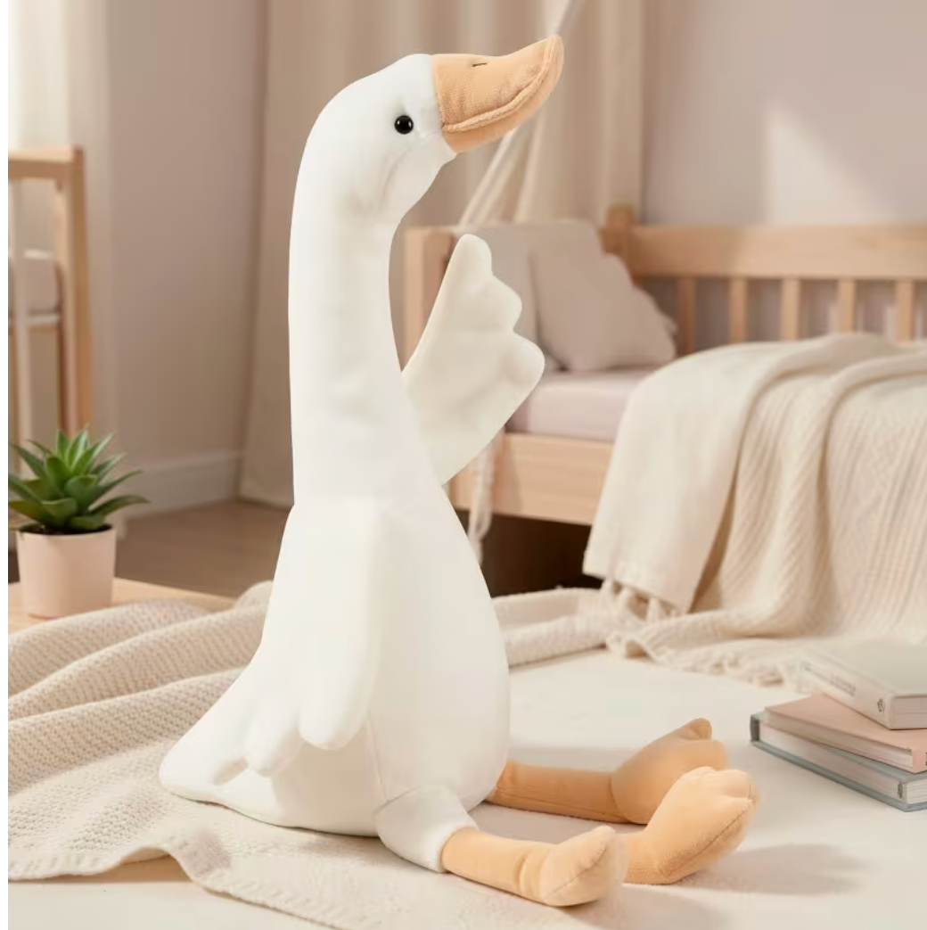 Soft long-neck goose plush sitting on a bed in a cozy bedroom reading nook.