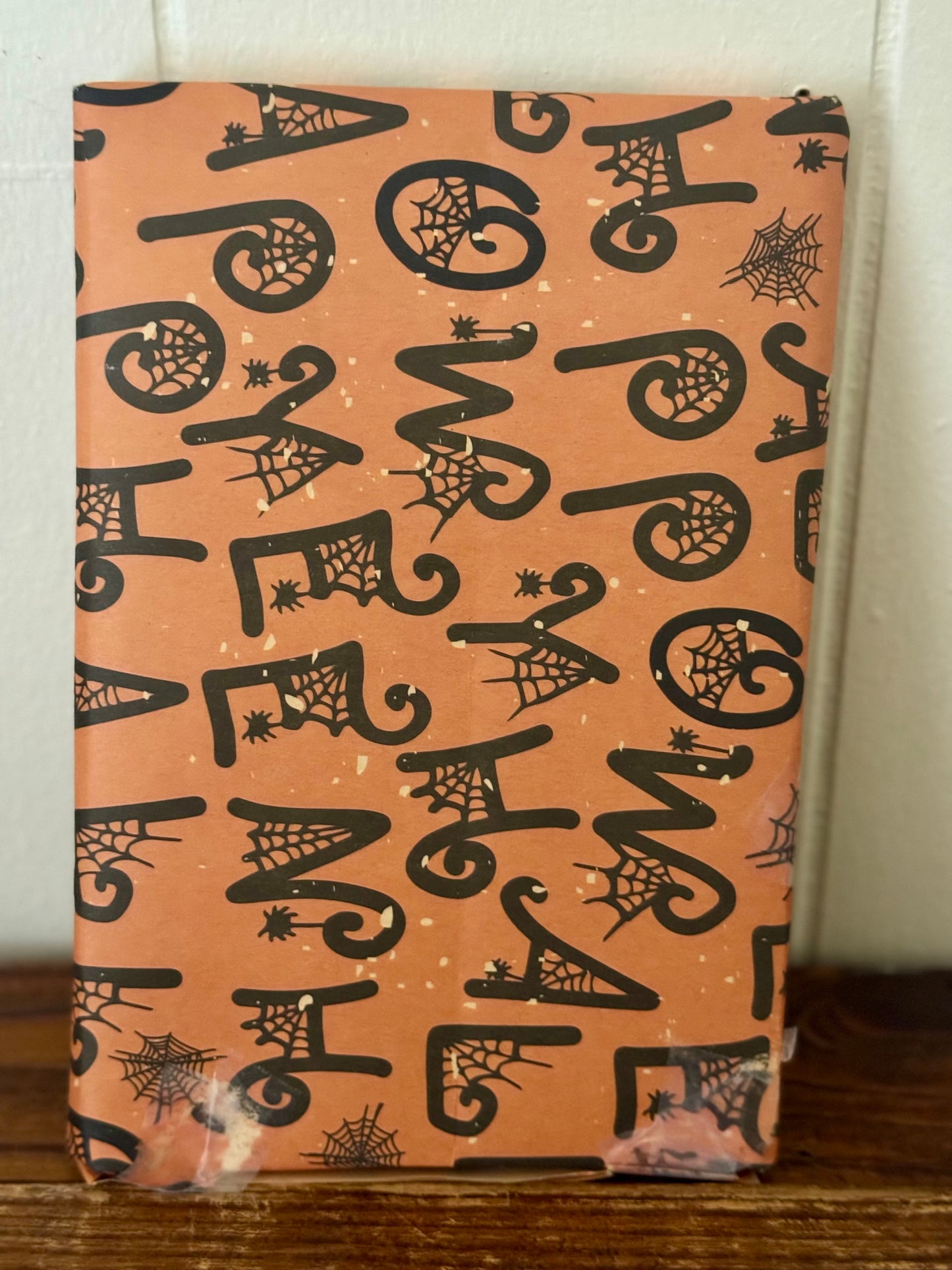 Halloween-themed wrapping paper with black text and graphics on a peach background.