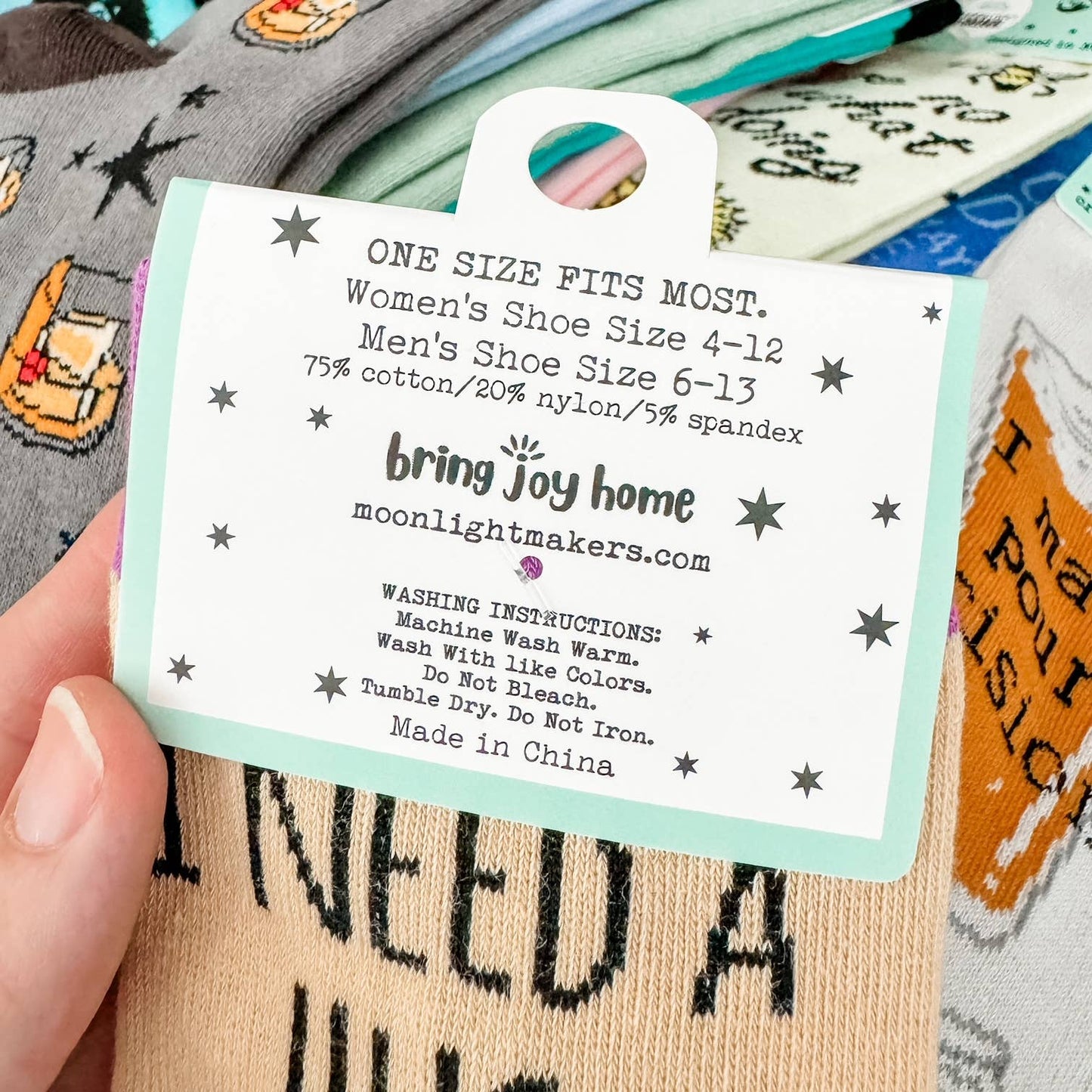 Close-up of the back of a Moonlight Makers crew socks hang tag showing one size fits most, women’s shoe size 4–12, men’s shoe size 6–13, 75% cotton 20% nylon 5% spandex, and washing instructions.