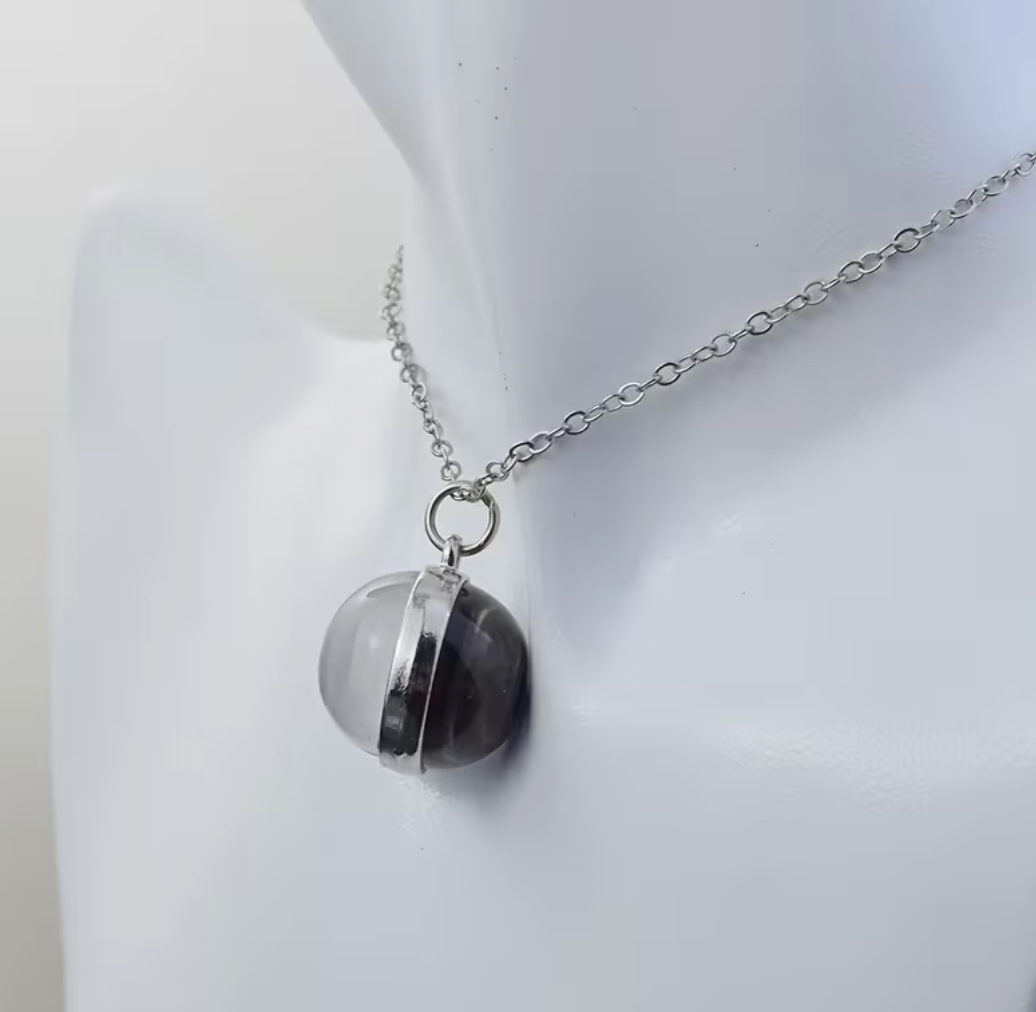 A silver chain necklace with a round pendant made of two stacked translucent discs, one clear and one dark gray/black, displayed on a white mannequin bust.