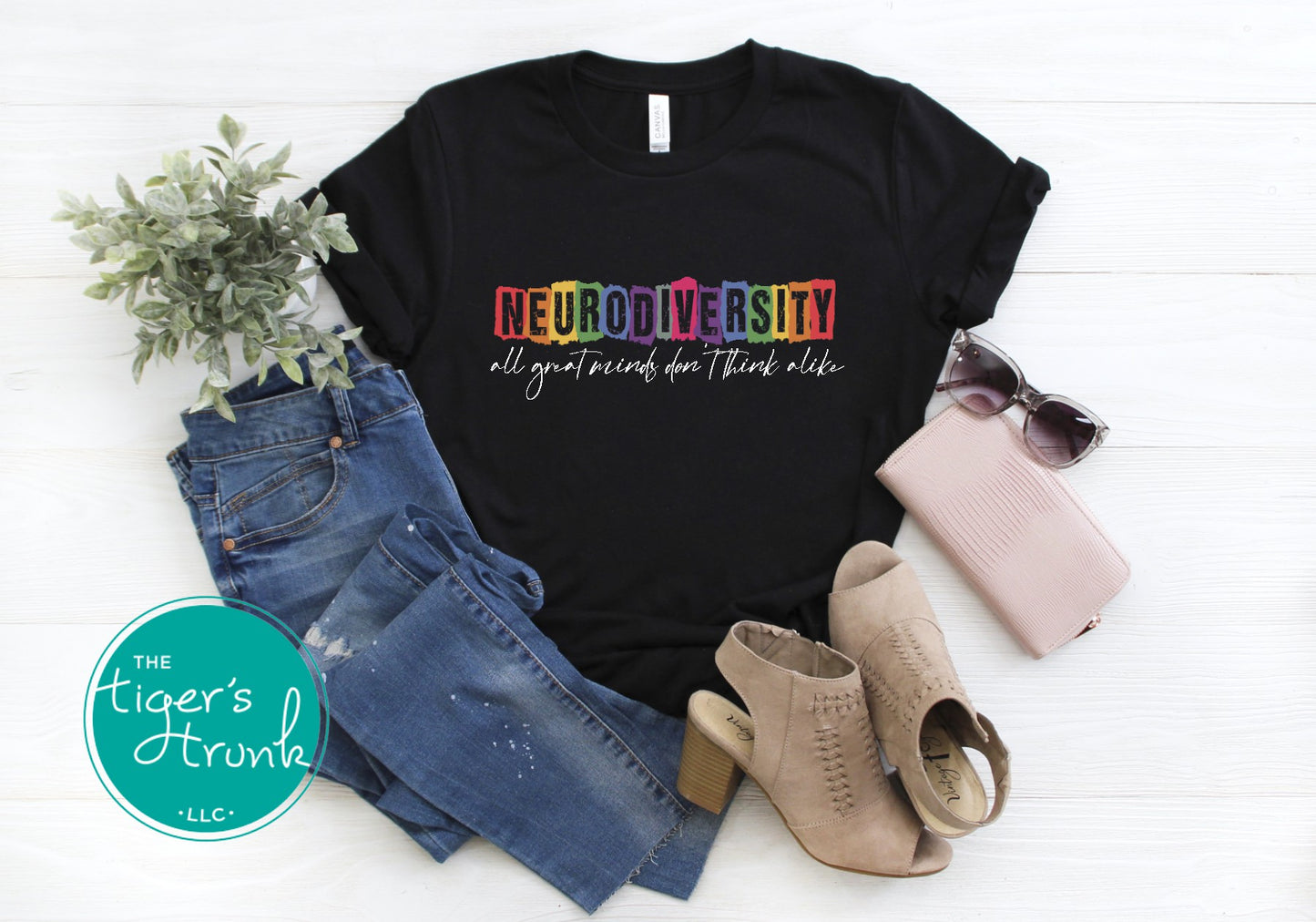 A white graphic tee with the phrase 'Neurodiversity All Great Minds Don't Think Alike' printed on the front, displayed with denim shorts, patterned socks, and a pair of sunglasses.