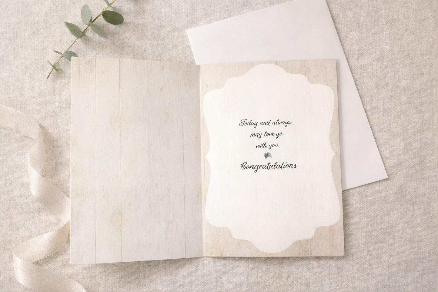 Open wedding greeting card showing inside message that reads Today and always may love go with you, Congratulations, styled on a neutral linen flat lay with white envelope, ribbon, and eucalyptus.