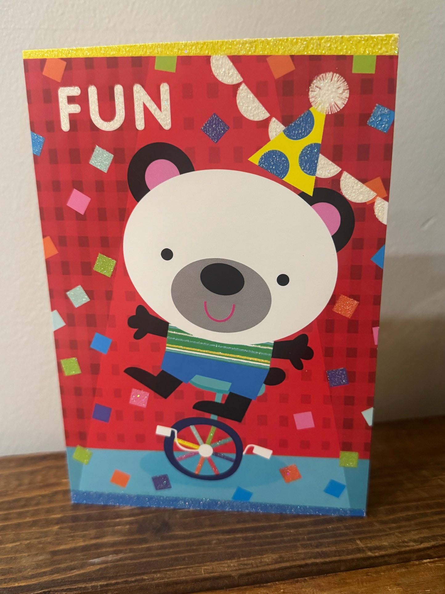 A playful birthday card featuring a unicycling panda with glitter accents and the word Fun on the front.