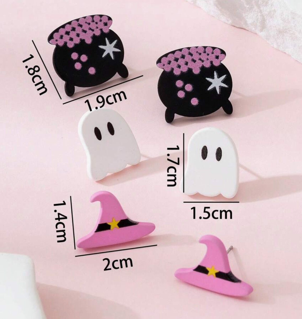 Set of Halloween-themed earrings including ghosts, witch hats, and cauldrons with measurements on a pink background.