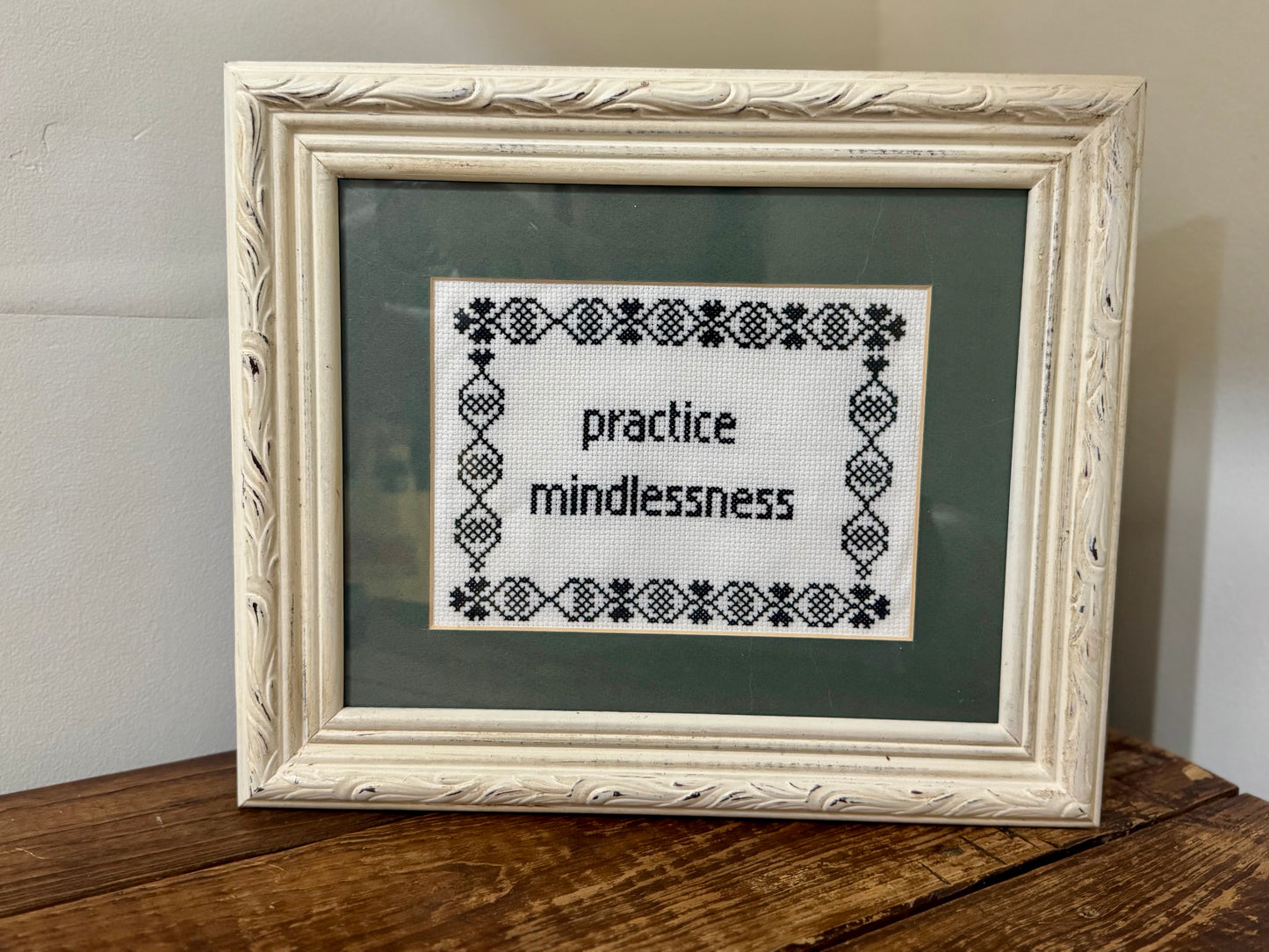 Framed 8x10 cross-stitch featuring the phrase Practice Mindlessness in hand-stitched embroidery.